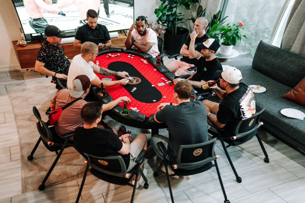 Players around a poker table with red felt in a modern room
